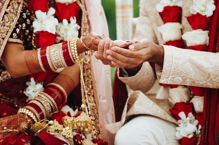 Hands of an Indian bride and groom intertwined for a wedding ritual.